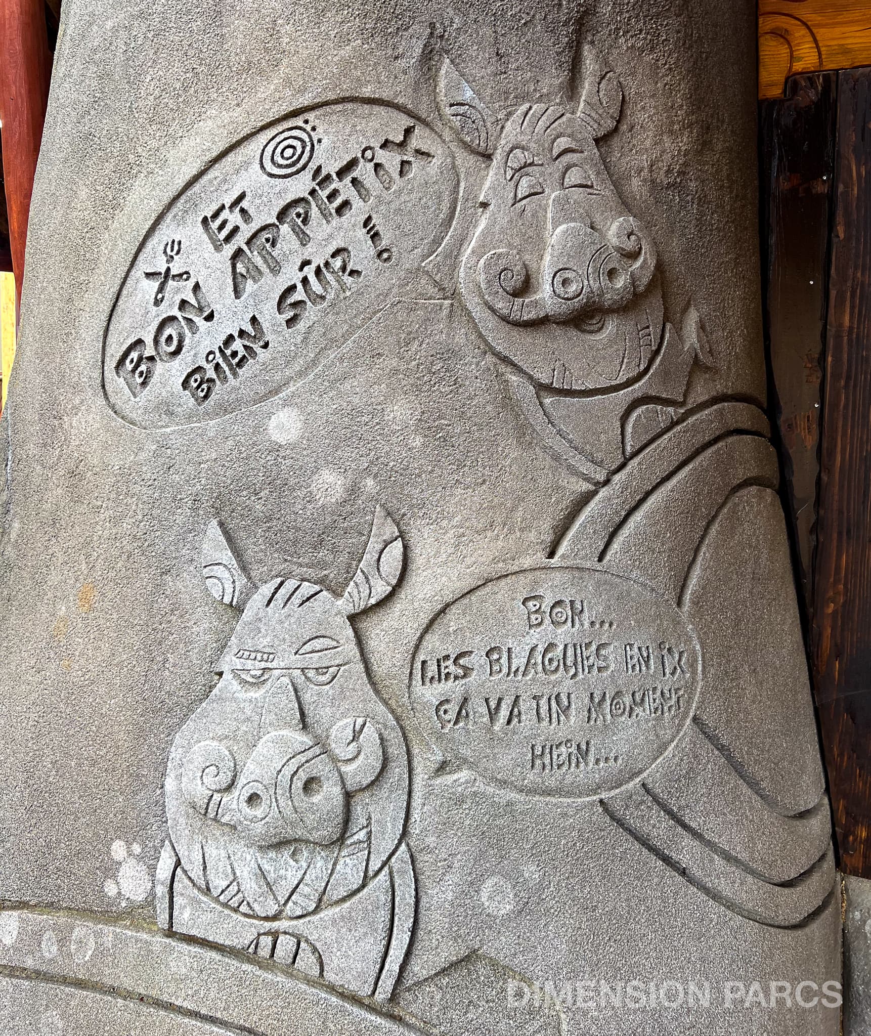 Menhir sculpté représentant deux sangliers. L'un dit "Et bon appétix bien sûr", l'autre répond "Bon... Les blagues en ix ça va un moment hein...'