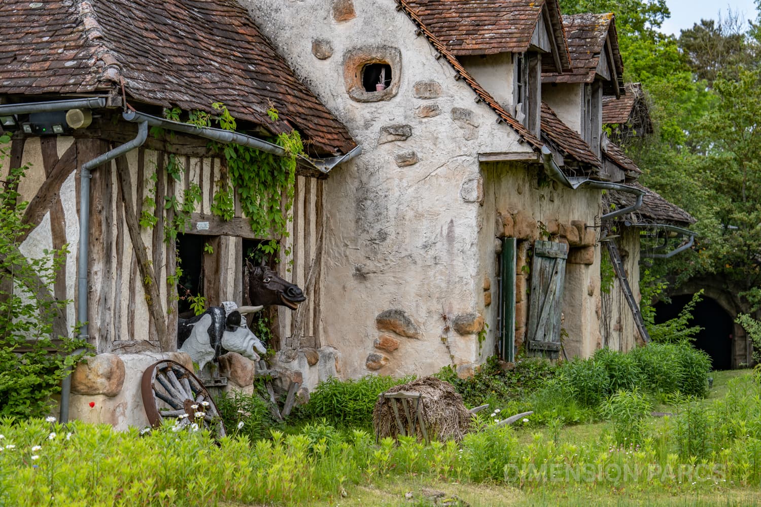 Extérieur de la ferme de l'attraction Nationale 7 au Parc Astérix. Une vache et un cheval sont dans leur écurie.